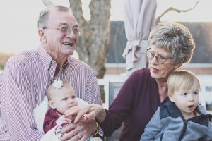 happy elderly couple holding grandkids outside